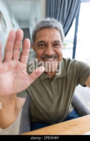 Primo piano ritratto di un uomo anziano biraciale allegro che agita la mano mentre parla con la videochiamata Foto Stock