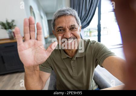 Primo piano ritratto di un uomo anziano biraciale sorridente che agita la mano mentre parla con una videochiamata Foto Stock