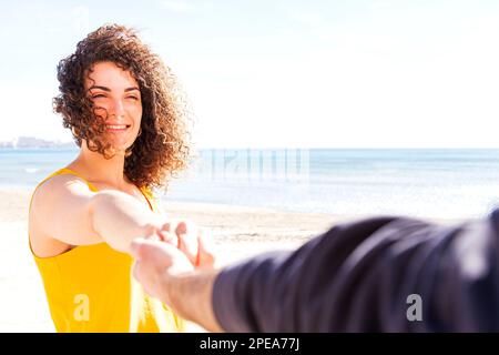 Vista POV del tipo di raccolto che tiene le mani con allegra femmina Soulmate sulla spiaggia sabbiosa contro il mare in estate Foto Stock