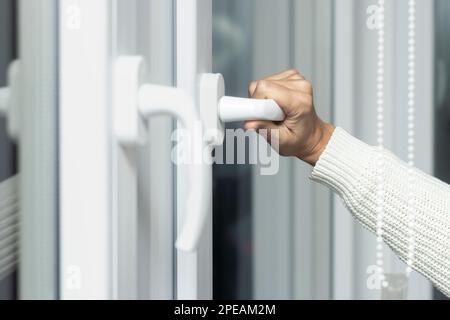 Il primo piano della mano di una donna apre una finestra bianca di plastica per ventilare. Foto Stock