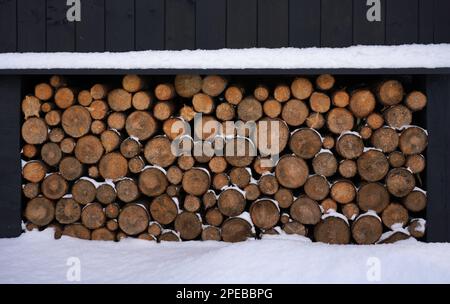 Legna da ardere accatastata sotto casa con tempo nevoso Foto Stock