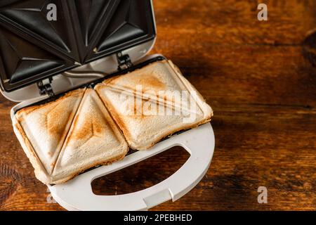 Panini appena sfornati in una macchina per sandwich su uno sfondo di legno. Concetto di colazione mattutina. Foto Stock