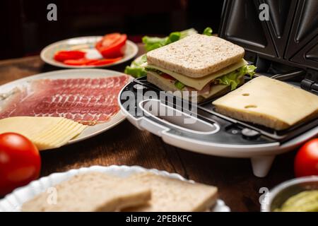 Cottura di panini con farciture diverse. Paninoteca e vari ingredienti su sfondo di legno. Foto Stock