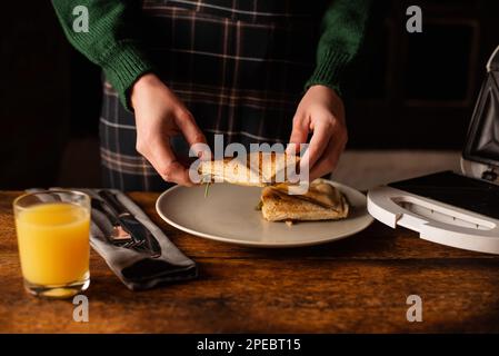 Donna irriconoscibile prende un toast panino su uno sfondo di legno. Colazione al mattino, snack, dieta. Foto Stock