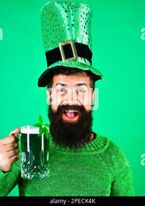 Felice uomo bearded in leprechaun cappello bere birra nel pub o bar. Festa di San Patrizio. Uomo sorridente con un bicchiere di birra verde. Bevanda verde Foto Stock