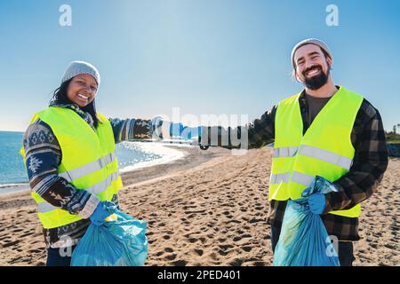 Due volontari multirazziali battendo pugni dopo aver raccolto rifiuti e la sporcizia di plastica dalla sabbia sulla spiaggia. Un paio di attivisti ambientali sorridenti in piedi guardando la telecamera. Concetto di ecologia. Foto di alta qualità Foto Stock