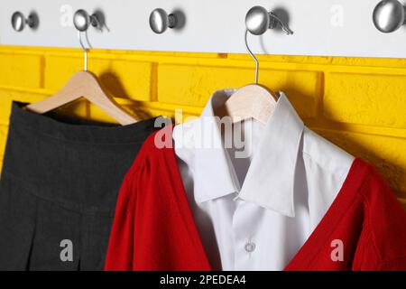 Camicia, jumper e gonna appesi alla parete di mattoni gialli. Uniforme scolastica Foto Stock