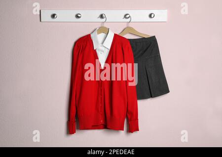 Camicia, jumper e gonna appesi alla parete rosa. Uniforme scolastica Foto Stock