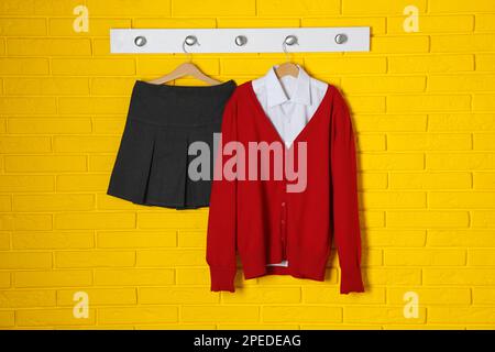 Camicia, jumper e gonna appesi alla parete di mattoni gialli. Uniforme scolastica Foto Stock