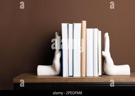 Bellissimi libri a forma di mano con libri su scaffale vicino a parete marrone Foto Stock