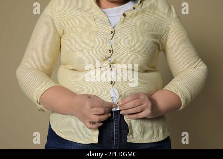 Donna sovrappeso cercando di buttare su camicia stretta su sfondo beige, primo piano Foto Stock