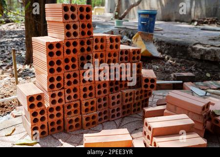 Pila di mattoni cavi arancioni con attrezzi di posa di mattoni in un cantiere. Palo di mattoni di creta bruciati nuovi preparato per lavoro di muratura Foto Stock