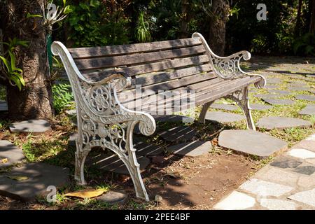 Vecchia panca stagionato in legno e metallo in un parco in una giornata di sole. Panca bianca elegante in un giardino senza persone intorno Foto Stock