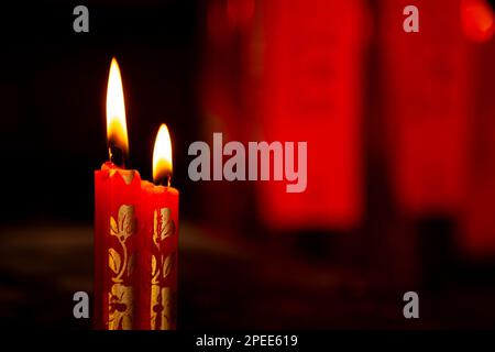 2 candele rosse, decorate con motivi floreali d'oro, in un tempio taoista cinese. Due candele di cera che bruciano in una stanza buia Foto Stock