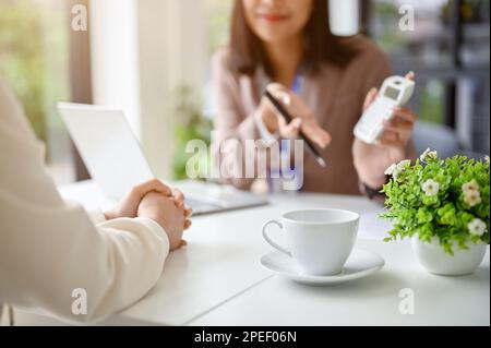 Immagine ritagliata di professionista asiatico banchiere femminile o consulente finanziario parlare con un cliente femminile in ufficio. Foto Stock
