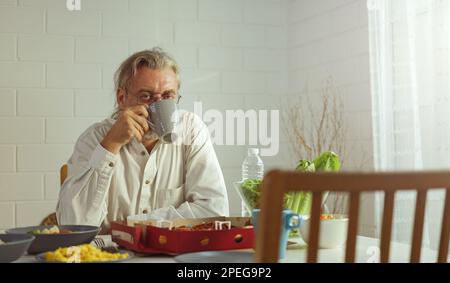 Anziano nonno in pensione rimanere a casa con il viso infelice seduta da solo sul tavolo da pranzo in casa. Depresso anziano maturo anziano rovesciato sentirsi solo Foto Stock