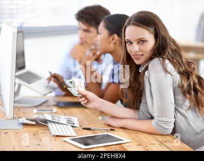 Lavorare insieme per scegliere le immagini corrette per i propri clienti. Tre giovani redattori che guardano le foto nel loro ufficio. Foto Stock