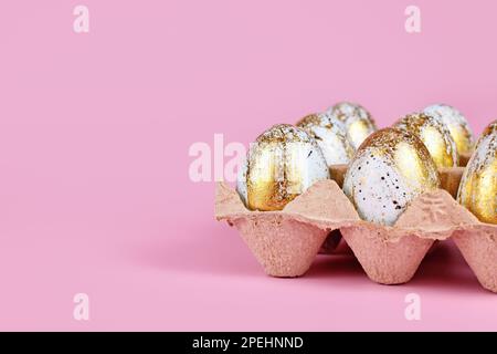 Uova di Pasqua dipinte blu con macchie dorate in scatola di uova su sfondo rosa con spazio copia Foto Stock