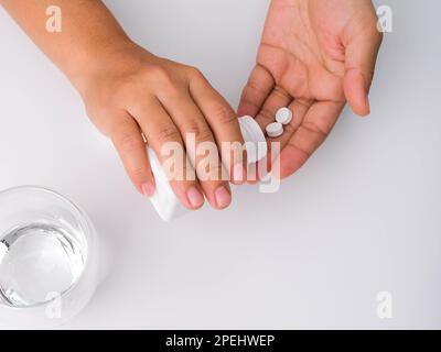 Primo piano di una donna che versa pillole dal flacone per scopi medicinali. Donna che tiene pillole in mano con l'acqua. Sanità, medicina, trattamento, terapia c Foto Stock