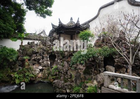 Un tranquillo giardino asiatico caratterizzato da un ponte di pietra che attraversa un tranquillo laghetto circondato da una lussureggiante vegetazione Foto Stock