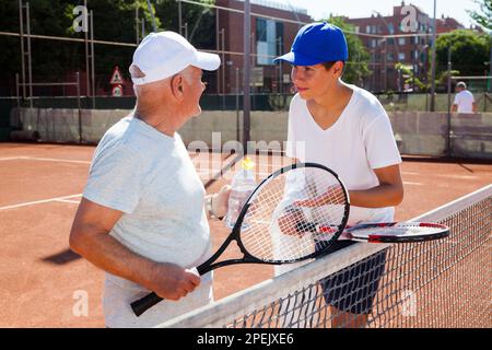 nonno e nipote parlano sul campo giocando a tennis Foto Stock