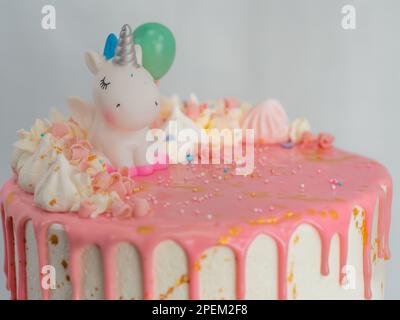 torta di compleanno bianca glassata rosa con unicorno, meringa e spolverate i toppers, pennellate di vernice commestibili dorate sul supporto Foto Stock