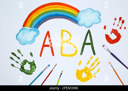 Abbreviazione disegnata ABA (Applied Behavior Analysis), arcobaleno, stampe di palma e pennelli su carta bianca, piano Foto Stock