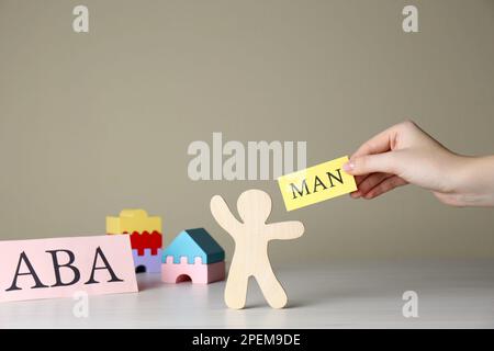 Donna tenendo carta con parola uomo vicino figura umana e abbreviazione ABA (Applied Behavior Analysis) a tavola di legno bianco, primo piano Foto Stock