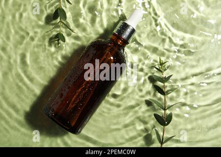 Bottiglia di olio idrofilo e ramoscelli di piante in acqua su fondo verde chiaro, piatto Foto Stock