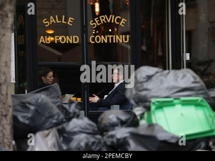 Parigi, Francia. 15th Mar, 2023. Si pranza in un ristorante di fronte al quale si trovano pile di rifiuti sulla strada di Parigi, Francia, 15 marzo 2023. È probabile che i rifiuti continuino ad accumularsi nella capitale, poiché i raccoglitori di rifiuti e i pulitori di strada saranno in sciopero fino a marzo 20. Secondo il municipio, circa 76.000 tonnellate di rifiuti sono da raccogliere entro mercoledì a Parigi. Credit: Gao Jing/Xinhua/Alamy Live News Foto Stock