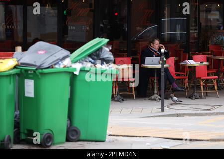 Parigi, Francia. 15th Mar, 2023. Un uomo prende un drink in un ristorante di fronte al quale si trovano mucchi di rifiuti sulla strada di Parigi, Francia, 15 marzo 2023. È probabile che i rifiuti continuino ad accumularsi nella capitale, poiché i raccoglitori di rifiuti e i pulitori di strada saranno in sciopero fino a marzo 20. Secondo il municipio, circa 76.000 tonnellate di rifiuti sono da raccogliere entro mercoledì a Parigi. Credit: Gao Jing/Xinhua/Alamy Live News Foto Stock