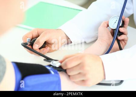 Vista ritagliata del medico maschile che controlla la pressione sanguigna del paziente al tavolo Foto Stock
