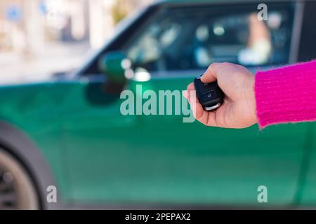 Taglia la femmina in maglione rosa premendo il pulsante sulla chiave dell'auto con telecomando mentre si apre il veicolo verde su sfondo sfocato Foto Stock