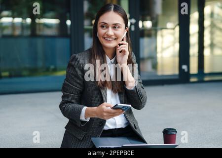 Giovane bella donna che lavora con il portatile utilizzando il telefono cellulare all'aperto, felice rilassante sentirsi bene al mattino. Comunicazione wireless. Donna Foto Stock