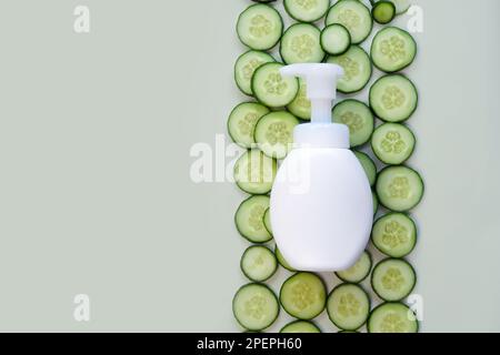Flacone per pompa cosmetica senza marchio sullo sfondo delle fette di cetriolo. Sapone liquido o bottiglia di crema detergente. Bottiglia per il marchio e l'etichetta. Confezione cosmetica Foto Stock