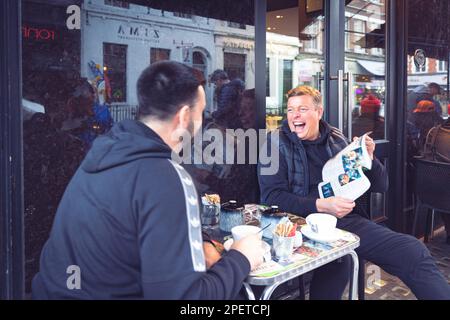 Thomas Henry Skinner l'uomo d'affari inglese e la personalità televisiva che legge Big Issue con un amico a Soho, nuvoloso inverno Londra, 2023 Foto Stock