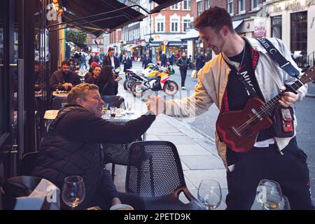 Thomas Henry Skinner l'uomo d'affari inglese e la personalità televisiva gode il giovane rapper ukelele a Soho, Liam C, inverno nuvoloso Londra 2023 Foto Stock