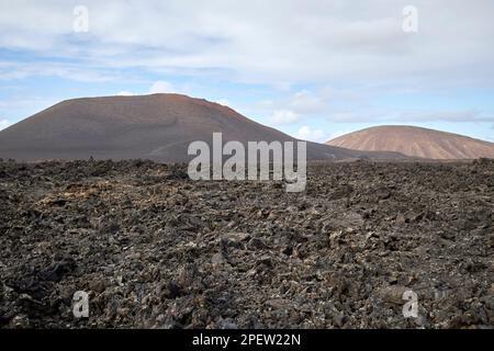 Guardando attraverso il campo di lava passato picon caldera coperta verso montana blanca arque nacional de timanfaya Lanzarote, Isole Canarie, Spagna Foto Stock