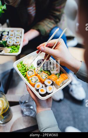 Un colpo verticale di persone che mangiano sushi da asporto con bacchette Foto Stock