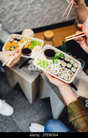 Un colpo verticale di persone che mangiano sushi da asporto con bacchette Foto Stock