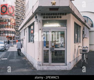 Una piccola vecchia signora che si fa strada davanti a una tipica casella di polizia urbana (koban/交番) vicino alla stazione di Sakuragicho nel centro di Yokohama, Giappone. Nota l'offico della polizia Foto Stock