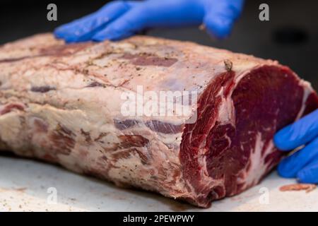 Una grande griglia di costola di manzo cruda su un tagliere di plastica industriale marrone. La carne è seduta sul banco della cucina di un ristorante. Foto Stock