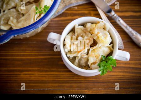 gnocchi cotti con patate e cipolle fritte, in una ciotola su un tavolo di legno. Foto Stock