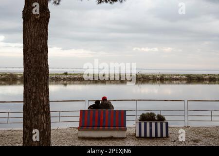 Una coppia seduta sulla panchina vicino al fiume Tago a Lisbona, Portogallo Foto Stock