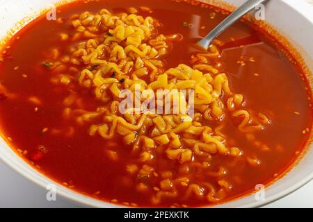 Zuppa di noodle piccante rossa in ciotola bianca, chiusura con texture Ramen e peperoncino piccante, cibo coreano piccante Foto Stock