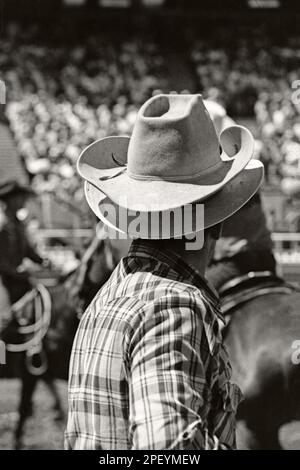 Ritratto monocromatico vintage di un cowboy rodeo che indossa due cappelli da cowboy al rodeo Calgary Stampede, intorno al 1980 Foto Stock