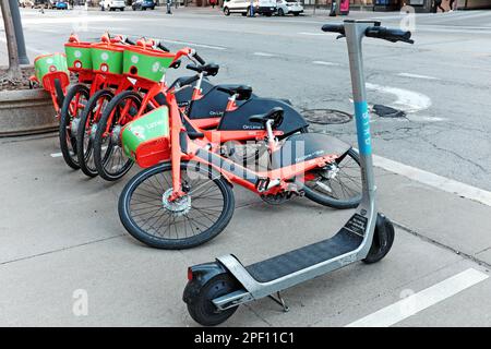 Un gruppo di sei biciclette elettroniche Lime sono parcheggiate su un marciapiede nel centro di Cleveland, Ohio, mentre uno scooter Lone Bird è parcheggiato nelle vicinanze. Foto Stock