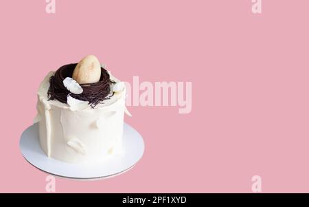 Elegante torta di pasqua decorata con nido di uccello al cioccolato, uova e piume. Sfondo rosa con spazio di copia. Orientamento orizzontale Foto Stock