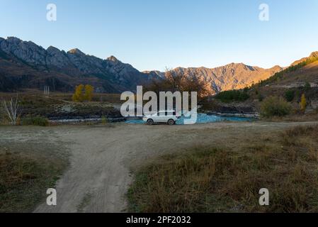 Un vecchio marchio di auto 'Honda HR-V' si trova in lontananza della strada sotto le montagne vicino al fiume in Altai in Siberia in serata. Altai, Russia Foto Stock