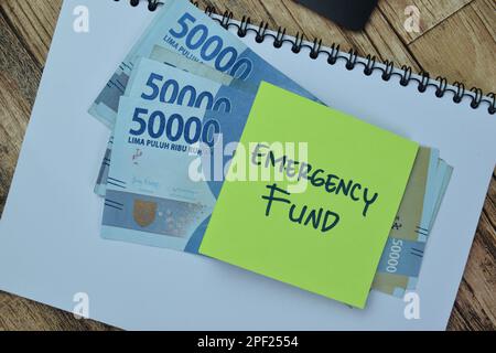 Concetto di Fondo di emergenza scrivere su note appiccicose con la valuta indonesiana isolato su tavola di legno. Foto Stock